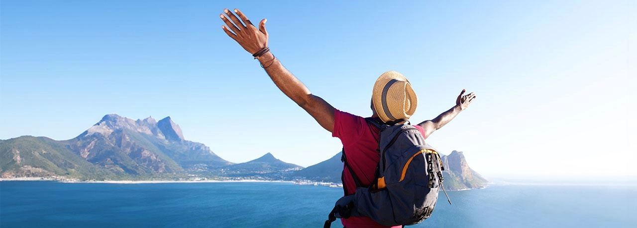 Man looking over coastal mountain range with arms extended